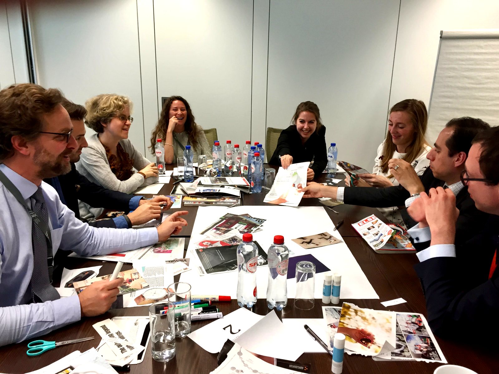 A #inextremis strategic workshop in Brussels: participants around a boardroom table building a mood board from printed cuttings, magazines and markers