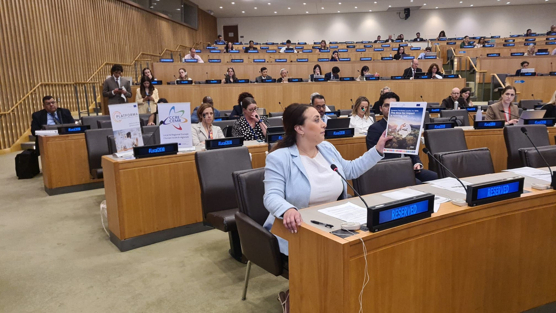 PLATFORMA and CCRE-CEMR representative holding up the European Territories Localise the SDGs report during a session at the United Nations