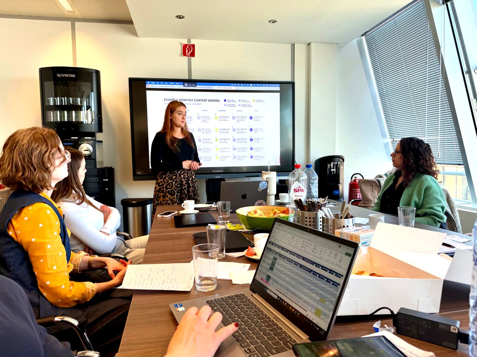 A #inextremis working session in Brussels: a team member presenting an example monthly content agenda on screen to colleagues around a meeting table
