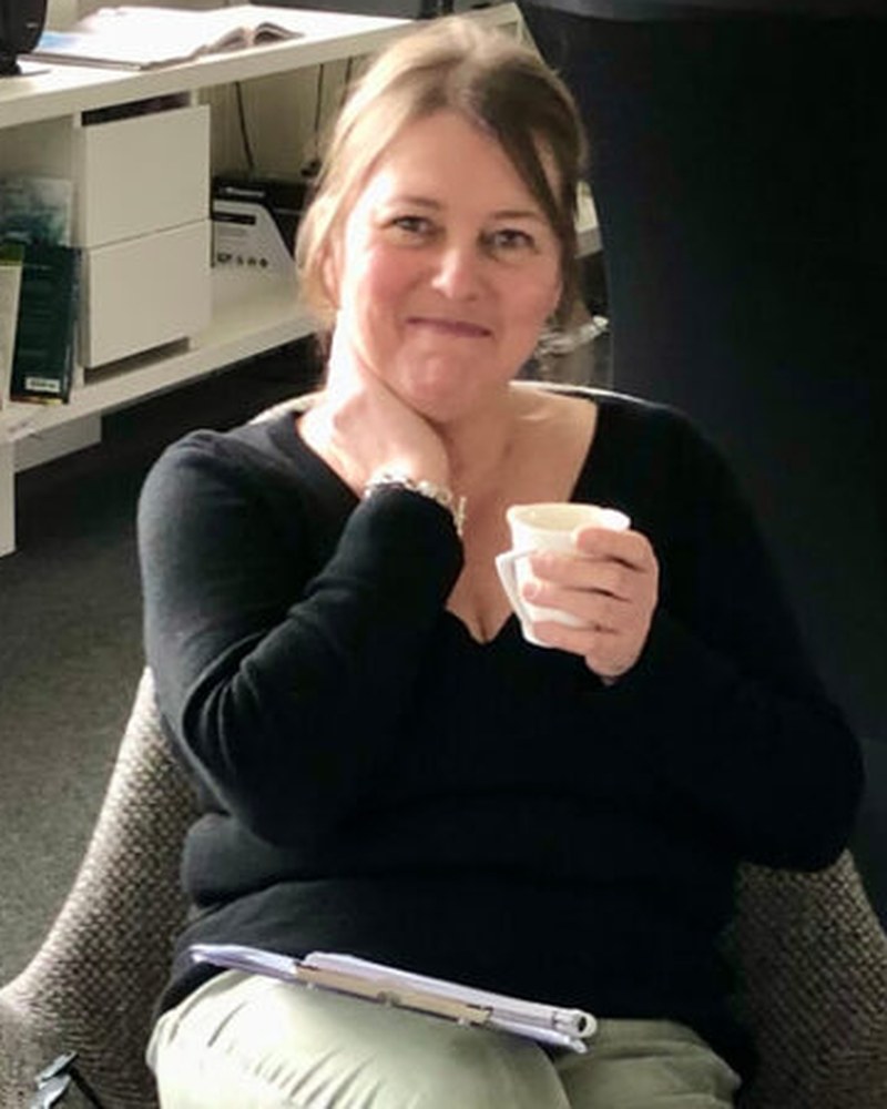 Corinne Guichart, co-founder and creative director of #inextremis, seated in the studio with a coffee and notebook